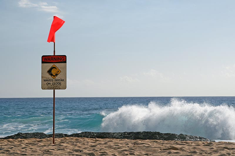 A sign warns beachgoers to be cautious of waves breaking on the ledge. Henry William Fu/Shutterstock.com